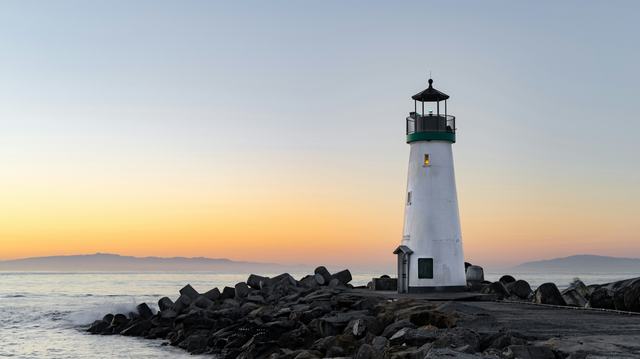 A photo of a lighthouse on the bay with the sun setting