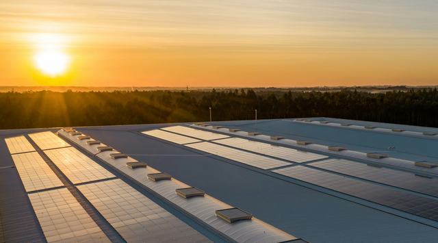 A photo of an array of solar panels on the top of a building with the sun setting