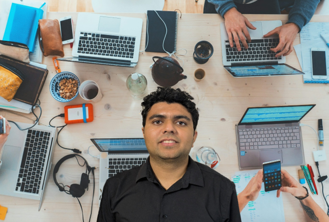 A photo of the EDC's Graduate Research Software Engineer with a background of people working on laptops on a desk